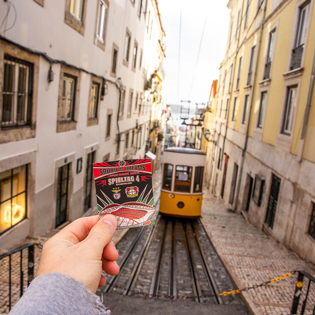 Sound-of-Dreams-Ticket zum 4. Spieltag, hochgehalten vor einer Straßenbahn in Lissabon