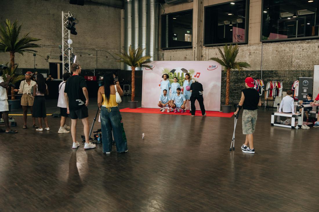 Industriehalle mit Palmen, Trikot-Rack und Ball-&-Beats-Fotowand mit Ortel-Logos, vor der Spieler posieren und