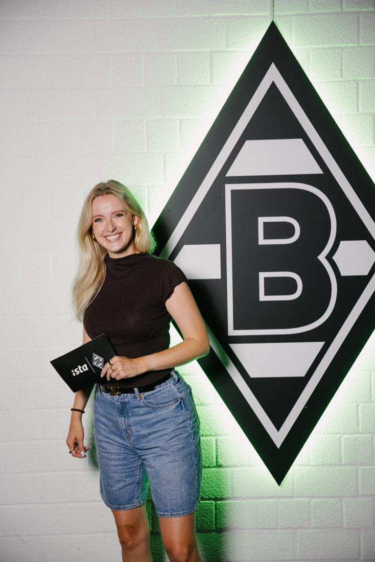 Creatorin hält die ista-x-Borussia-Einladungskarte vor der grün beleuchteten Raute – Detail der gestalteten Ei