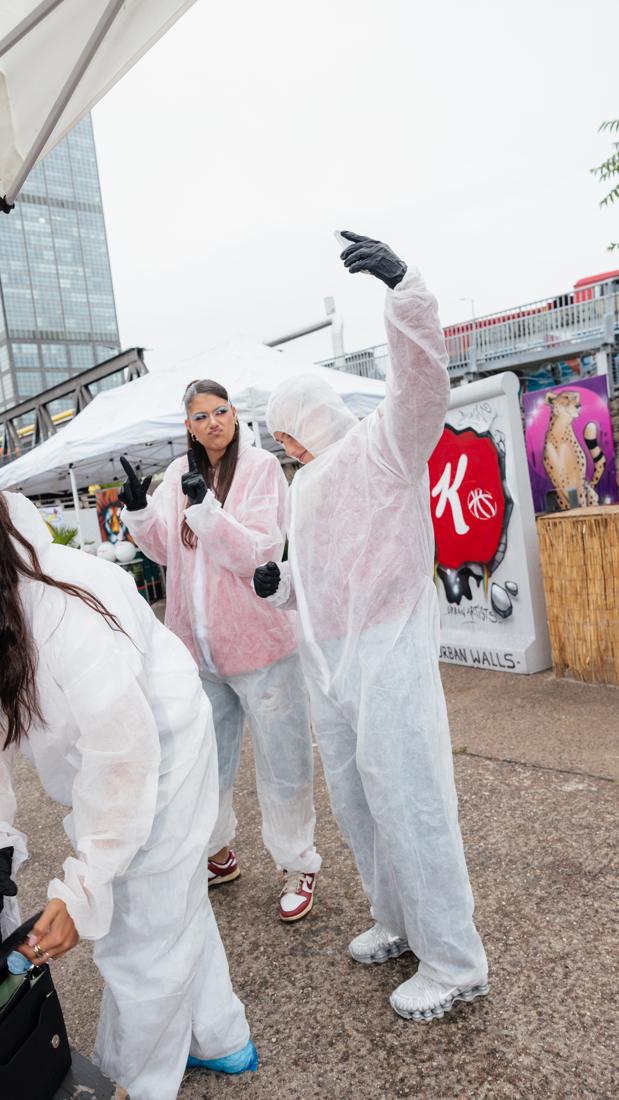 Creatorinnen in Maleranzügen posieren vor der gesprayten Kellogg's-K-Basketball-Wand, im Hintergrund Berliner